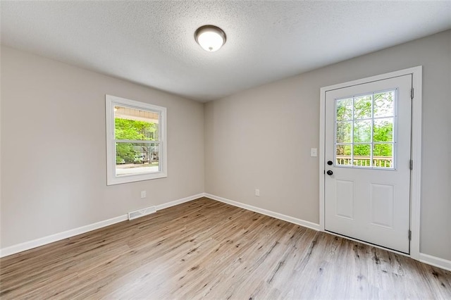 interior space featuring a textured ceiling, visible vents, light wood-style flooring, and baseboards