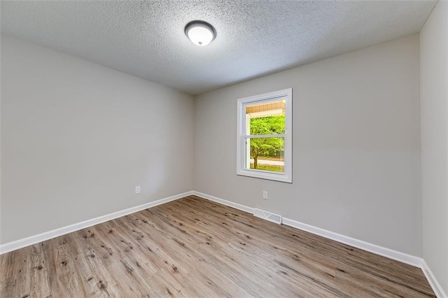 empty room featuring baseboards, visible vents, wood finished floors, and a textured ceiling