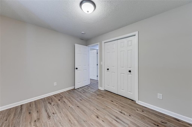 unfurnished bedroom with a textured ceiling, wood finished floors, a closet, and baseboards
