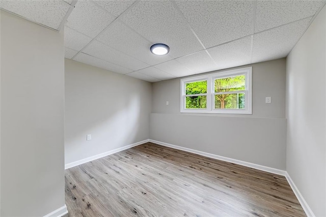 spare room with a drop ceiling, wood finished floors, and baseboards