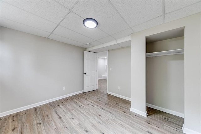 unfurnished bedroom with a paneled ceiling, a closet, wood finished floors, and baseboards