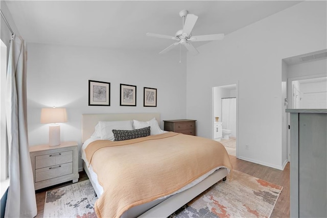 bedroom featuring ceiling fan, connected bathroom, light wood-type flooring, and vaulted ceiling