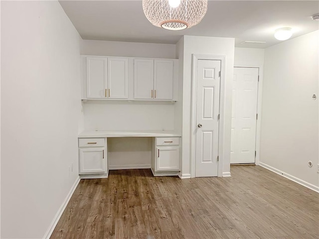 unfurnished office featuring built in desk, light wood-type flooring, and a notable chandelier