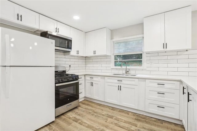 kitchen with white cabinets, light wood-style flooring, stainless steel appliances, light countertops, and a sink