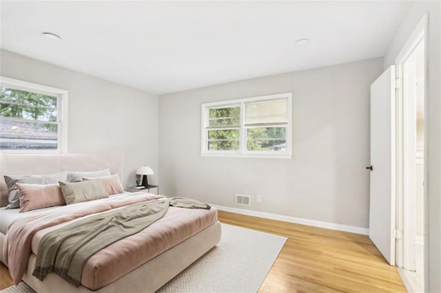 bedroom with baseboards, multiple windows, visible vents, and light wood-style floors