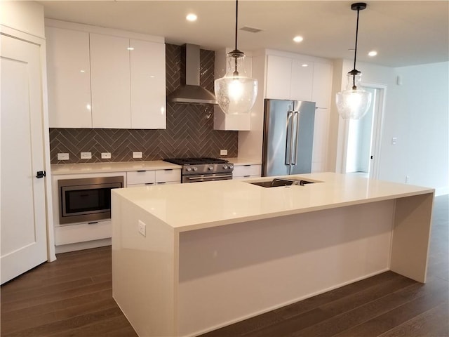 kitchen with pendant lighting, wall chimney range hood, a kitchen island with sink, and high quality appliances