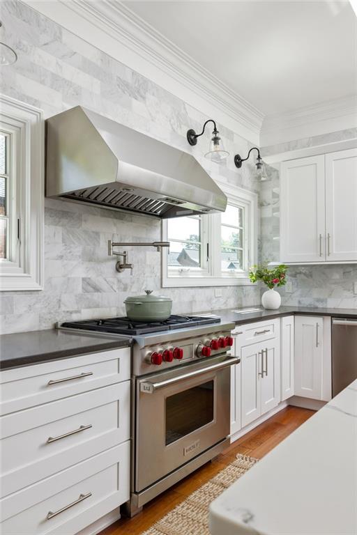 2015 N Decatur Rd NE, Atlanta, GA 30307 - kitchen featuring ornamental molding, wall chimney range hood, white cabinetry, stainless steel appliances, and decorative backsplash