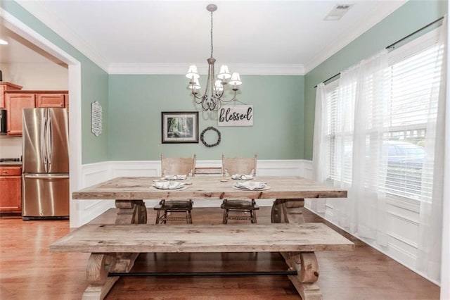 dining room featuring light wood finished floors, visible vents, crown molding, and a wainscoted wall