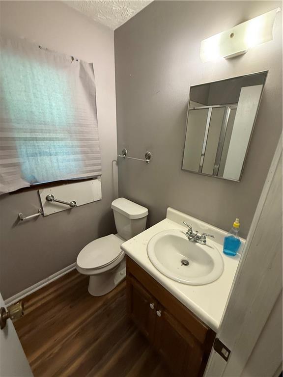 bathroom with vanity, toilet, a textured ceiling, wood finished floors, and a stall shower