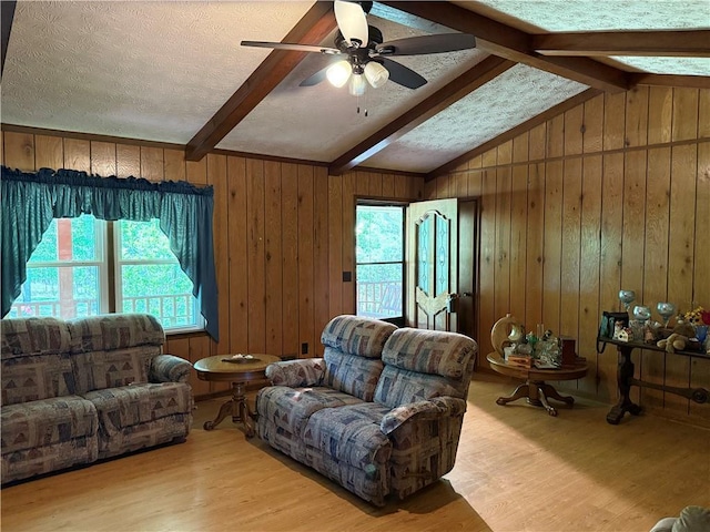 living area featuring wood finished floors, ceiling fan, wooden walls, a textured ceiling, and lofted ceiling with beams