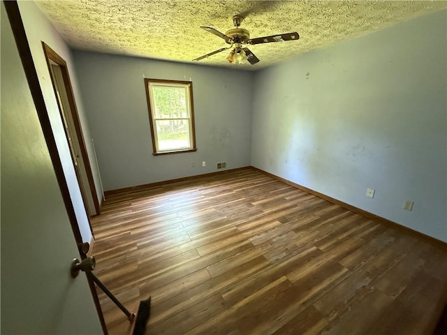 unfurnished room with visible vents, wood finished floors, baseboards, ceiling fan, and a textured ceiling