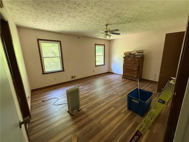 unfurnished bedroom with a ceiling fan, a textured ceiling, visible vents, wood finished floors, and baseboards