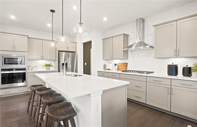 kitchen with decorative backsplash, stainless steel appliances, a center island with sink, and wall chimney range hood