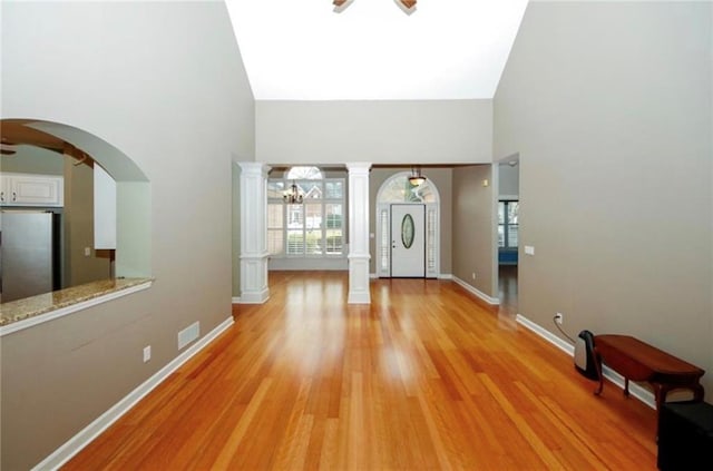 entryway featuring baseboards, light wood-style flooring, decorative columns, a high ceiling, and ceiling fan