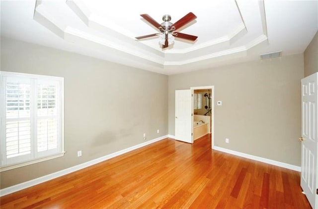 unfurnished bedroom featuring visible vents, crown molding, baseboards, light wood-type flooring, and a tray ceiling