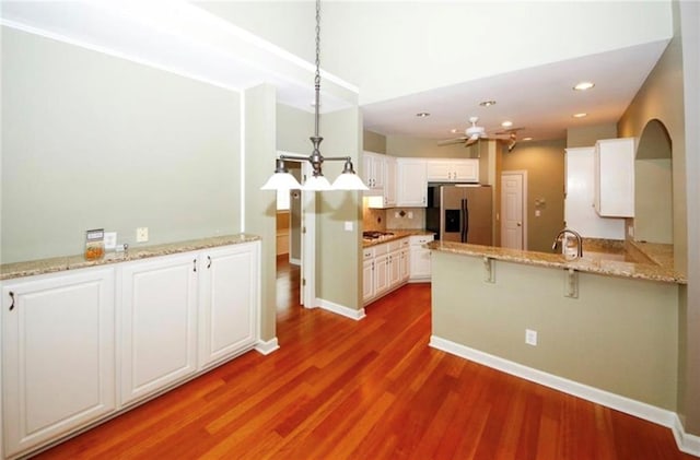 kitchen featuring stainless steel refrigerator with ice dispenser, wood finished floors, gas stovetop, white cabinetry, and a peninsula