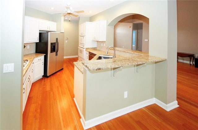 kitchen with a sink, arched walkways, stainless steel fridge with ice dispenser, light wood finished floors, and white oven