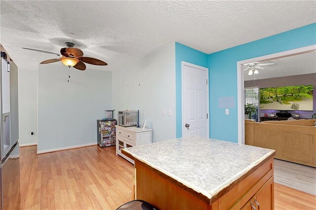 kitchen with a ceiling fan, light wood-style flooring, open floor plan, light countertops, and a textured ceiling