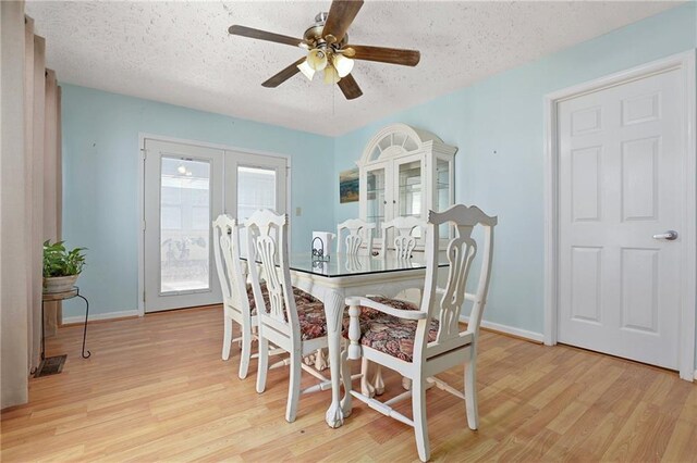 dining space featuring light wood-type flooring, a textured ceiling, a ceiling fan, baseboards, and french doors