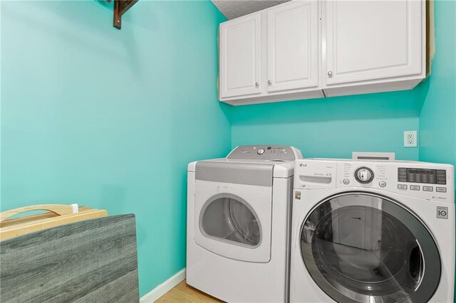 clothes washing area featuring cabinet space, washing machine and dryer, baseboards, and light wood-style flooring