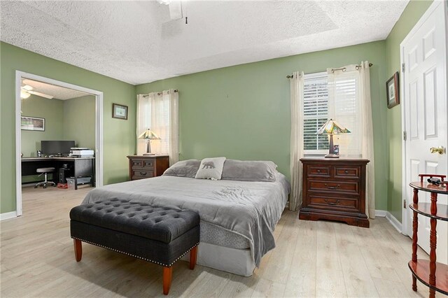 bedroom with a desk, a textured ceiling, light wood-style floors, multiple windows, and baseboards