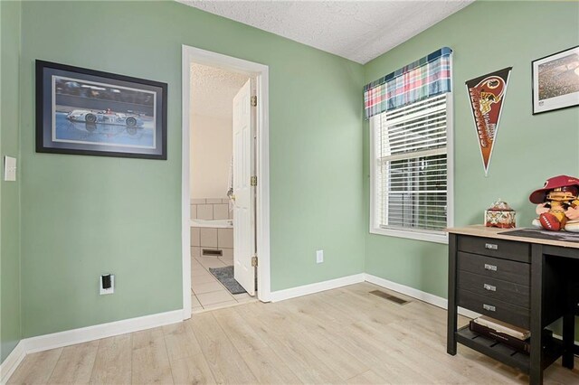 office area featuring light wood-style flooring, a textured ceiling, and baseboards