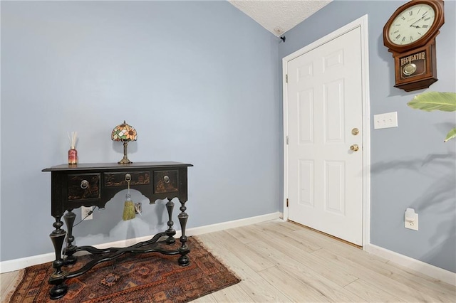 entrance foyer with light wood finished floors, baseboards, a textured ceiling, and vaulted ceiling
