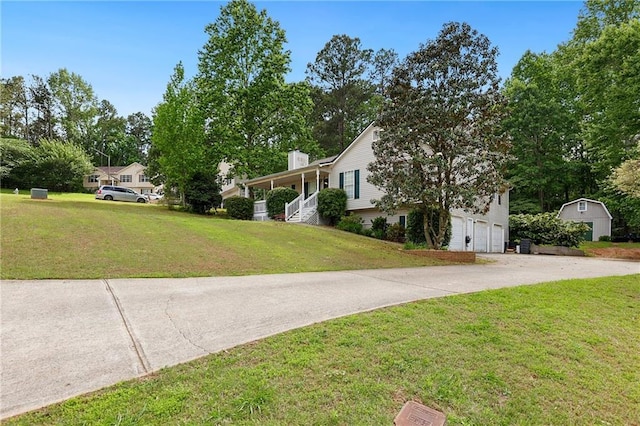 view of front of home featuring an attached garage, concrete driveway, a front lawn, a chimney, and an outbuilding