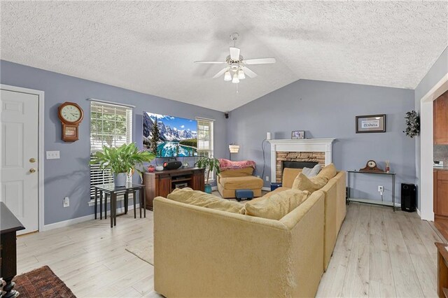 living area with ceiling fan, light wood-type flooring, vaulted ceiling, a fireplace, and a textured ceiling