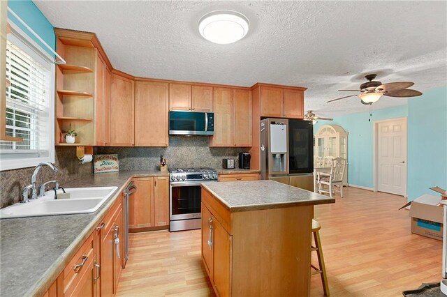 kitchen with appliances with stainless steel finishes, a sink, open shelves, light wood-style flooring, and a textured ceiling