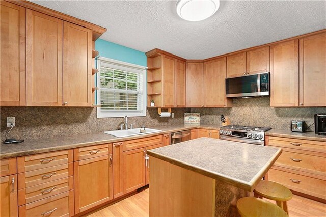 kitchen with appliances with stainless steel finishes, open shelves, a sink, a kitchen breakfast bar, and light wood-style flooring