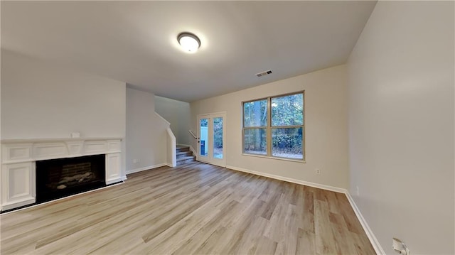 unfurnished living room with stairway, a fireplace, baseboards, and light wood finished floors