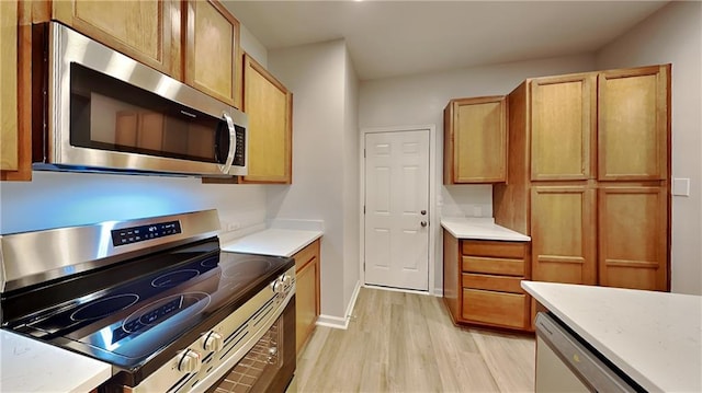 kitchen with light wood-style flooring, stainless steel appliances, light countertops, and baseboards