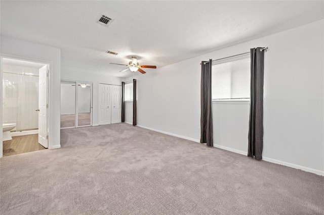 unfurnished bedroom with ceiling fan, two closets, light carpet, and ensuite bath