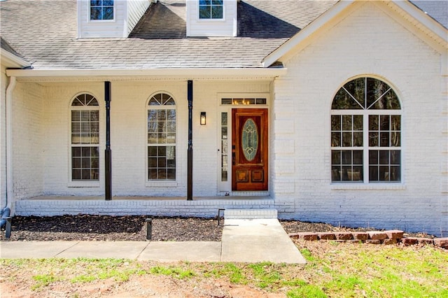 entrance to property featuring roof with shingles, a porch, and brick siding