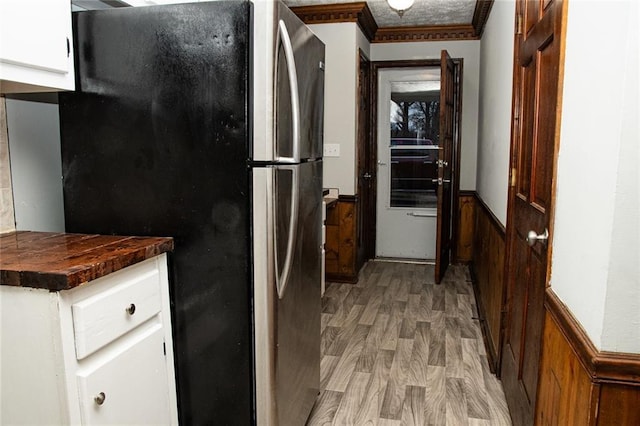 kitchen with wooden counters, wood walls, light hardwood / wood-style flooring, white cabinets, and stainless steel fridge