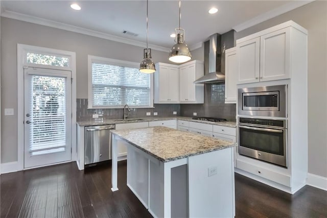 kitchen featuring a center island, appliances with stainless steel finishes, pendant lighting, wall chimney range hood, and white cabinets