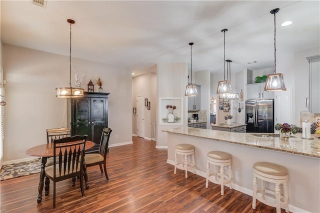 kitchen with kitchen peninsula, dark hardwood / wood-style flooring, a breakfast bar, stainless steel fridge with ice dispenser, and hanging light fixtures