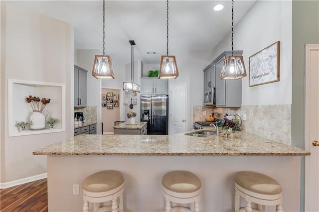 kitchen featuring light stone countertops, kitchen peninsula, pendant lighting, gray cabinets, and appliances with stainless steel finishes