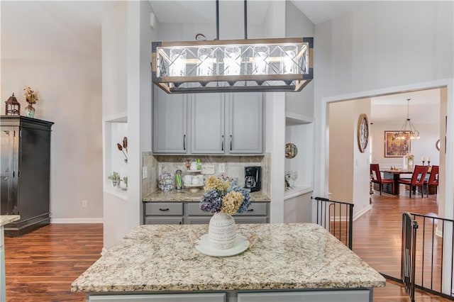 kitchen with gray cabinetry, tasteful backsplash, light stone counters, dark hardwood / wood-style floors, and decorative light fixtures