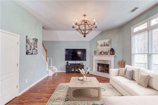 living room with a notable chandelier, dark hardwood / wood-style floors, a fireplace, and vaulted ceiling