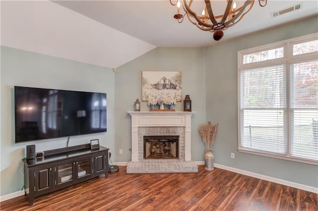 living room with a brick fireplace, hardwood / wood-style floors, vaulted ceiling, and a notable chandelier