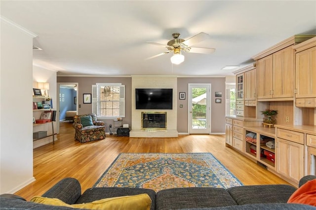 living area featuring crown molding, a ceiling fan, light wood finished floors, a brick fireplace, and baseboards