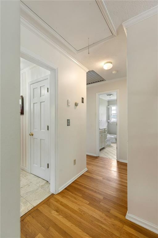 hallway featuring attic access, ornamental molding, light wood-style floors, and baseboards