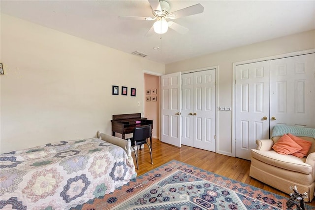 bedroom featuring two closets, wood finished floors, and a ceiling fan