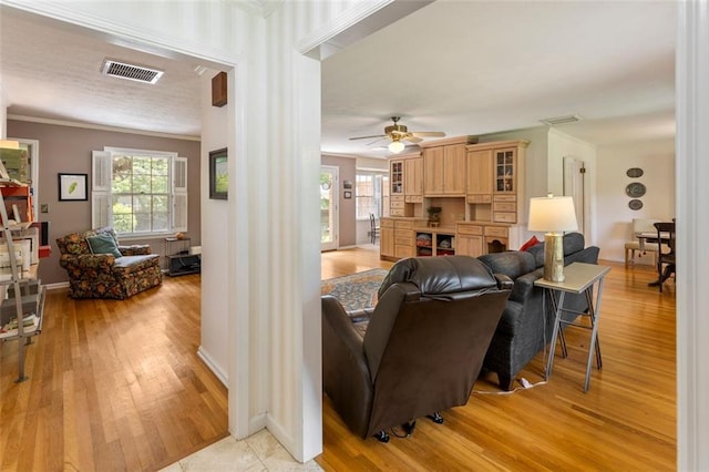 living room with light wood-style floors, ornamental molding, a ceiling fan, and baseboards