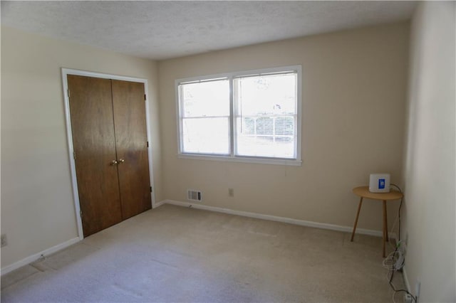 unfurnished bedroom featuring light carpet, a textured ceiling, and a closet