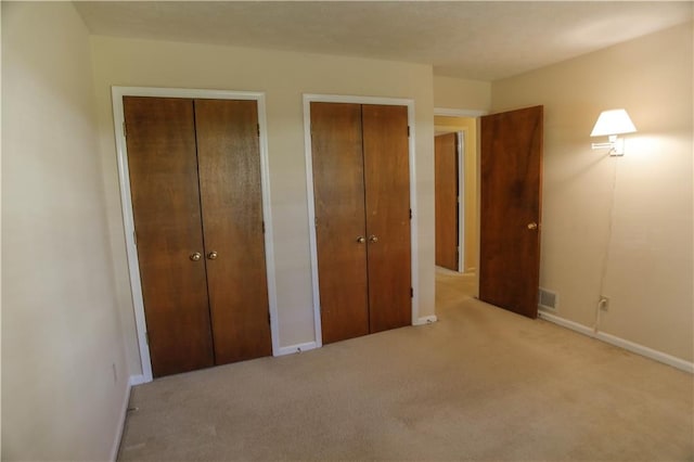 unfurnished bedroom with two closets and light colored carpet