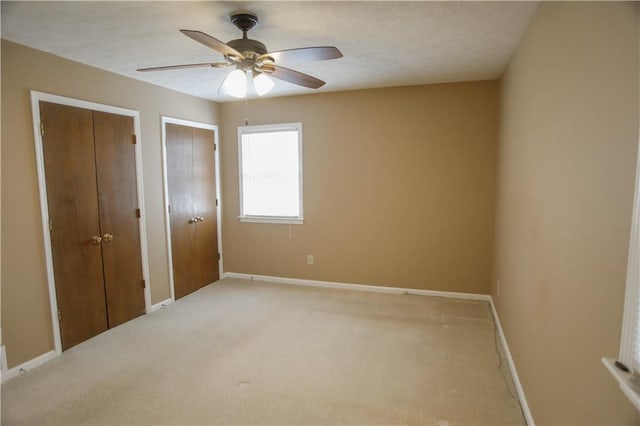 unfurnished bedroom featuring light carpet, two closets, and ceiling fan