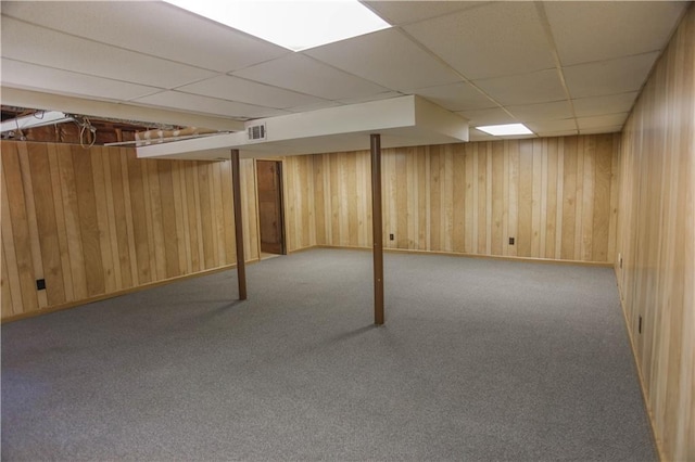 basement with light colored carpet, a drop ceiling, and wooden walls